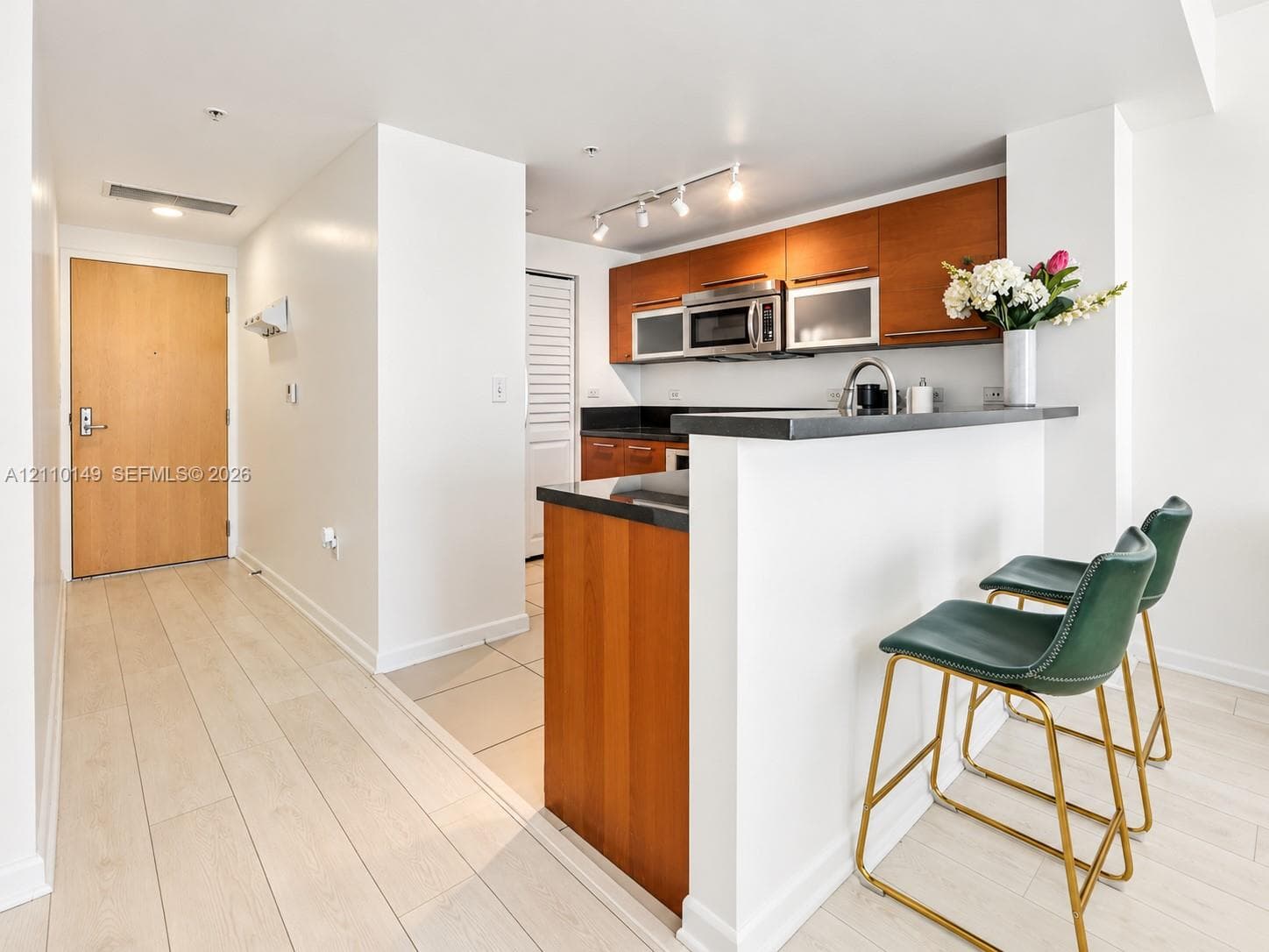Kitchen featuring wood-finish cabinetry, dark stone countertops, stainless steel appliances, and a breakfast bar with track lighting
