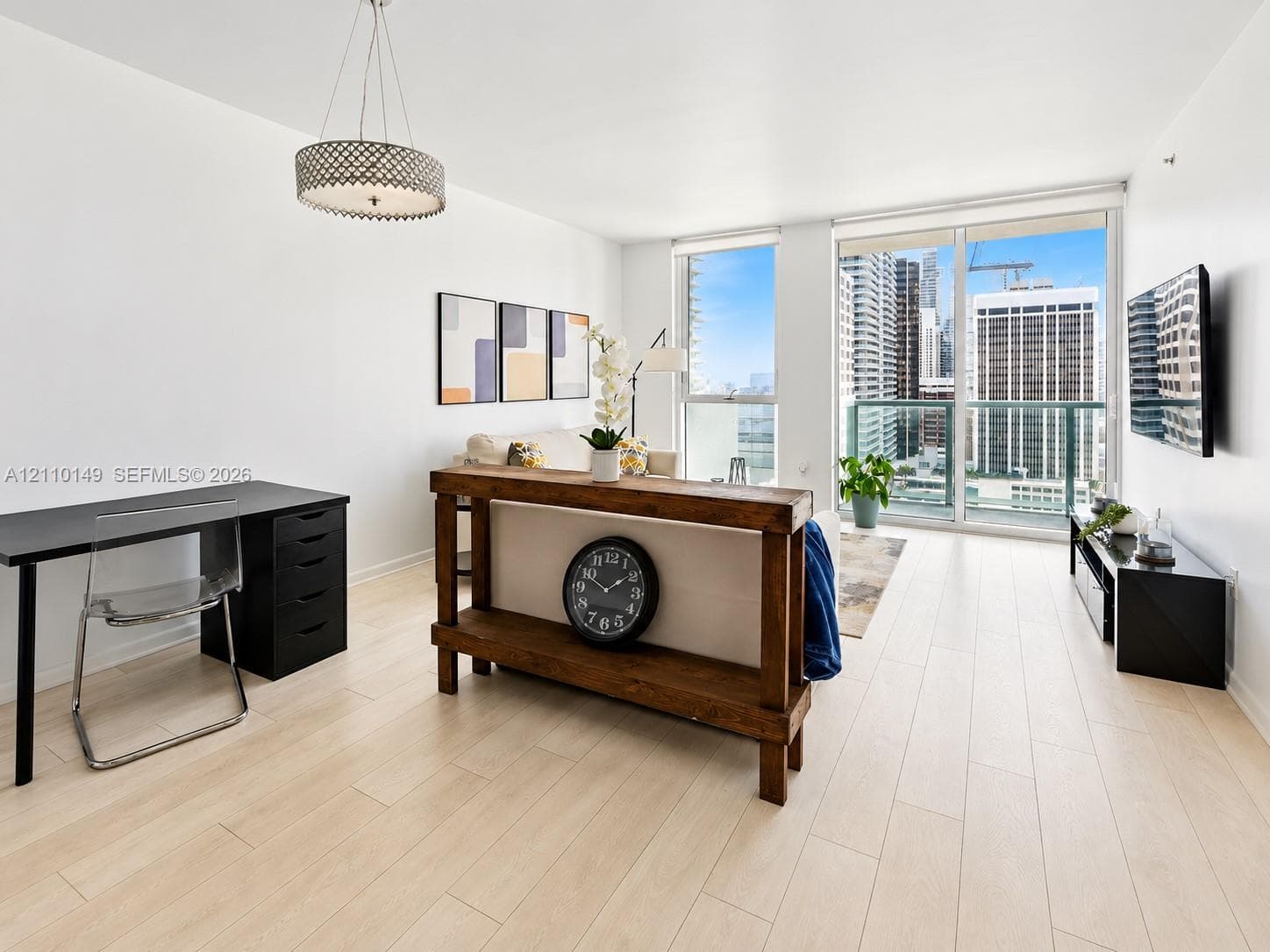 Light-toned wood-finish flooring, floor-to-ceiling windows, glass-panel balcony door, and a circular drum pendant light fixture