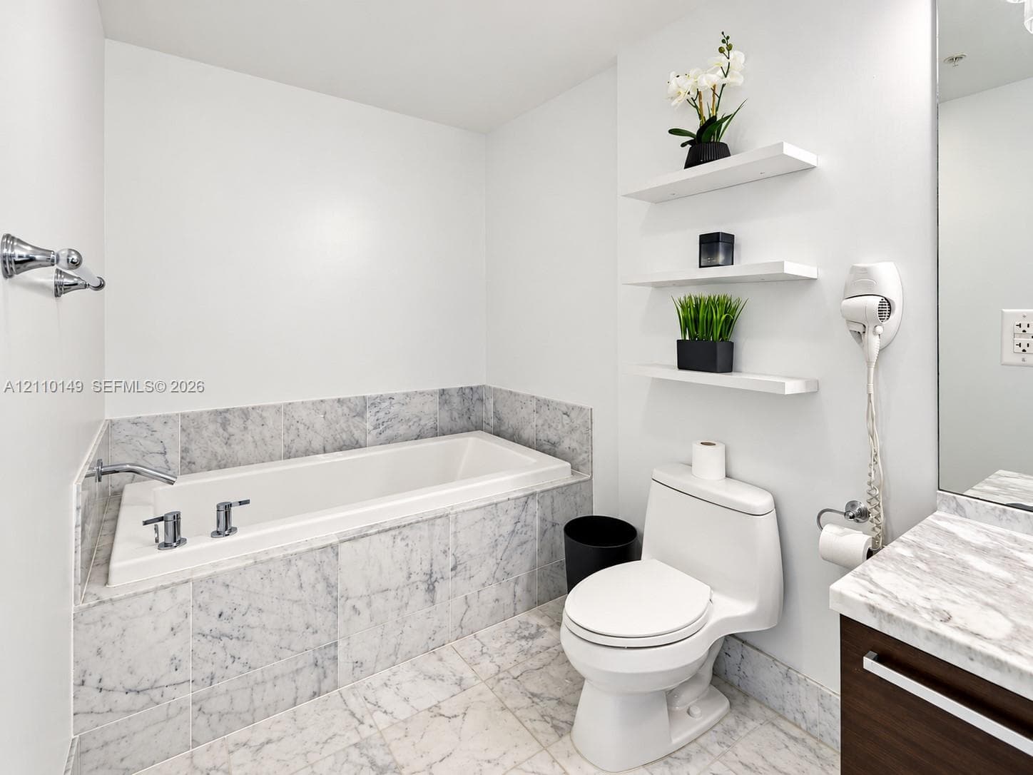 Bathroom featuring a stone-surround soaking tub, stone tile flooring, a vanity with a stone countertop, and three integrated wall-mounted shelves