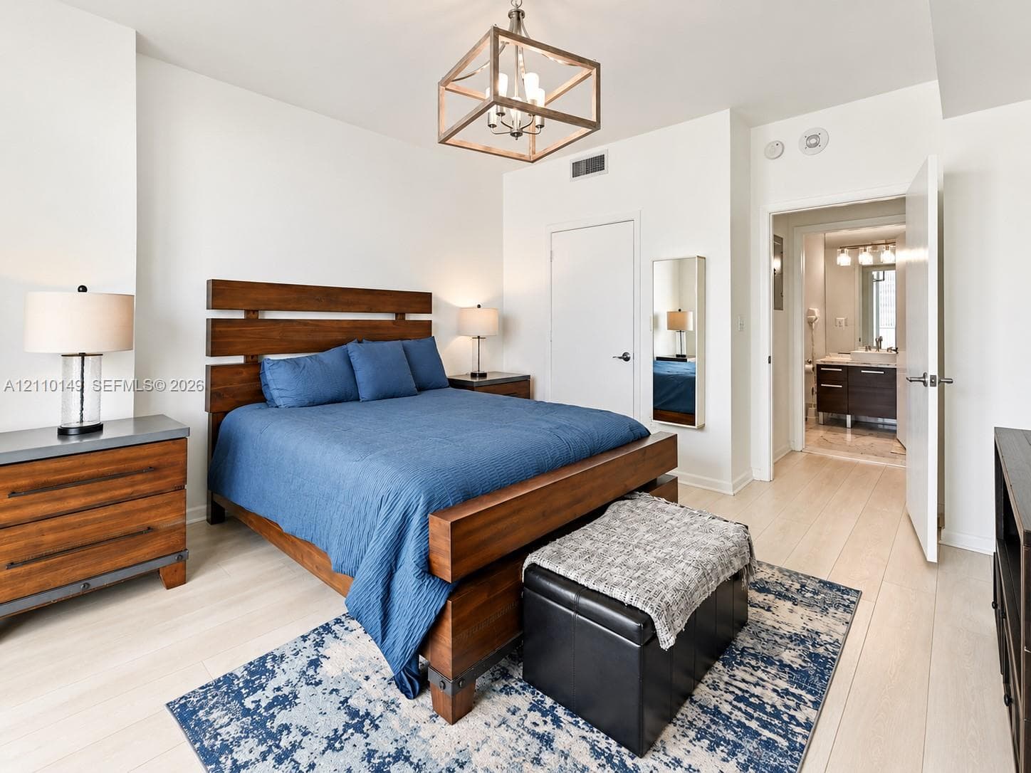 Neutral interior room featuring light wood-finish flooring, a geometric box-frame light fixture, and an integrated full-length wall mirror