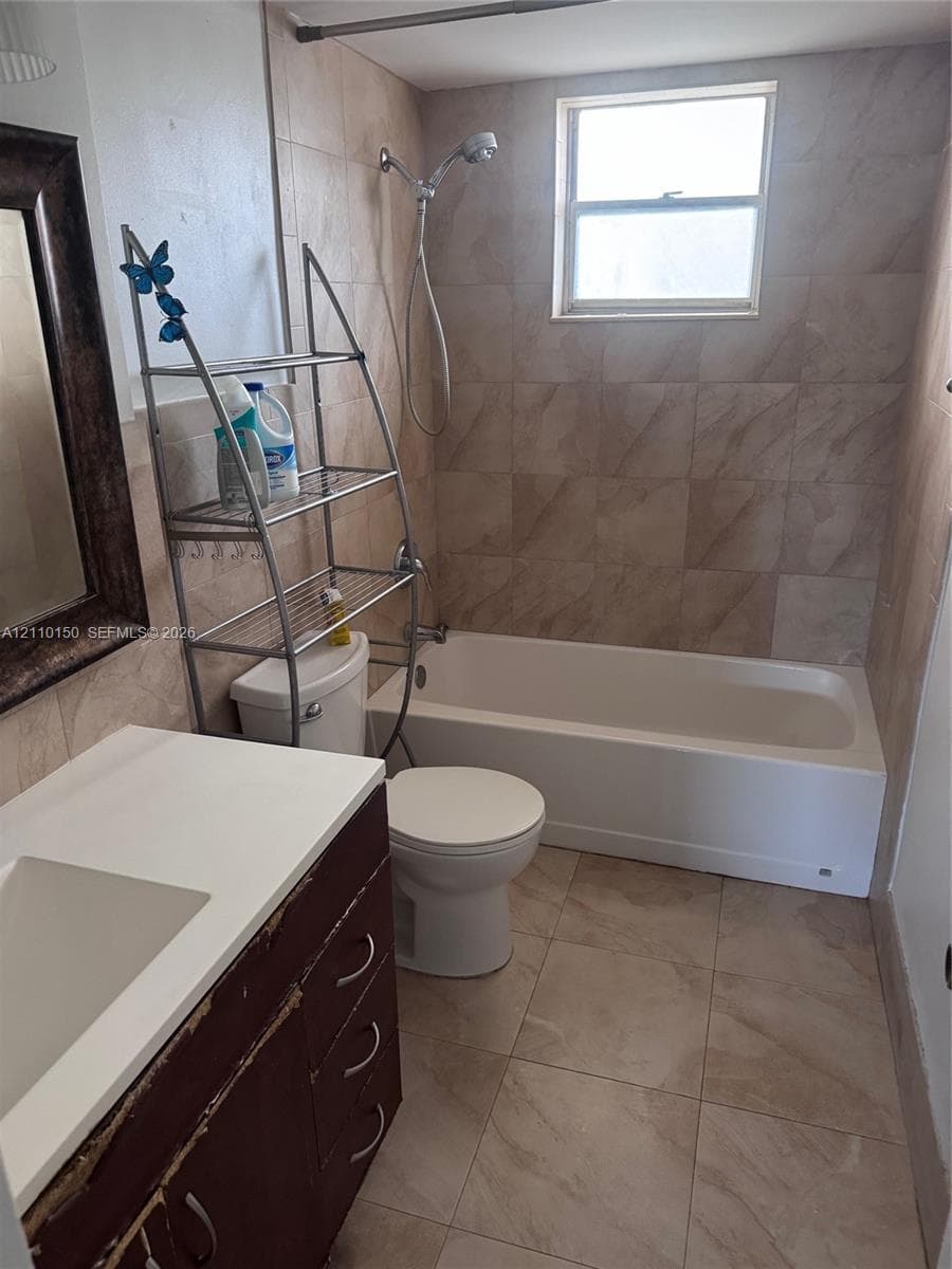 Bathroom featuring neutral-toned tile flooring, tub-shower combination with tiled surround, and vanity with a solid surface countertop