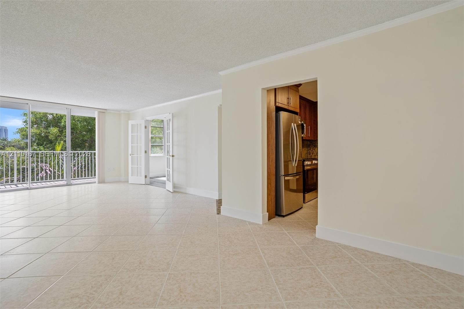 Spacious room featuring neutral tile flooring, floor-to-ceiling glass paneling, French doors, and stainless steel kitchen appliances