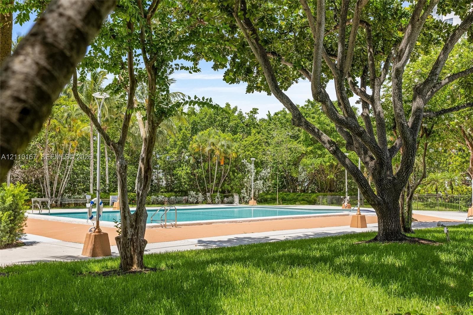 Swimming pool with a solid-surface deck, surrounded by mature trees, landscaping, and integrated lighting fixtures
