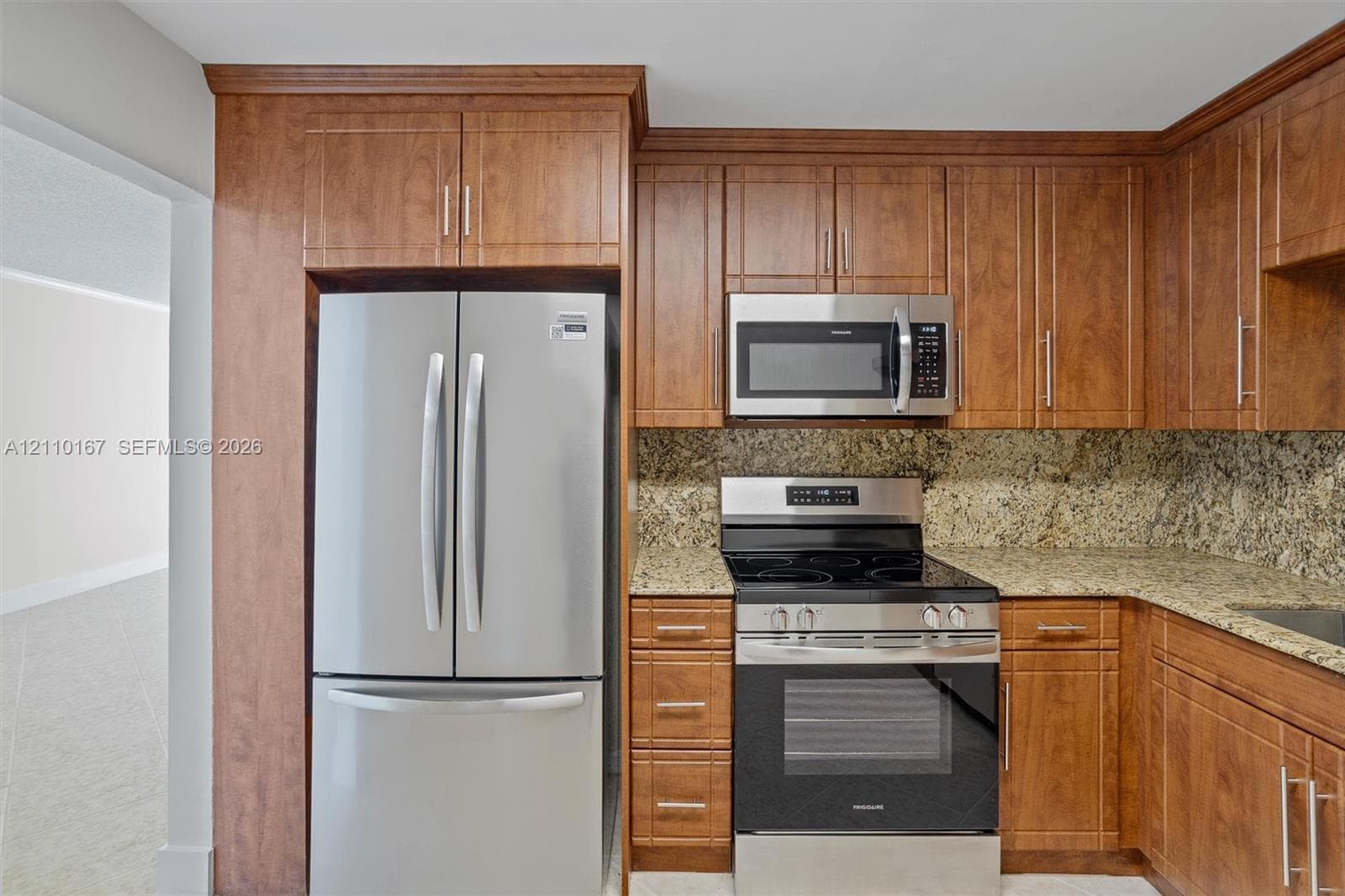 Kitchen featuring wood cabinetry, stone countertops, stone tile backsplash, and stainless steel appliances including a French door refrigerator, over-the-range microwave, and a slide-in range