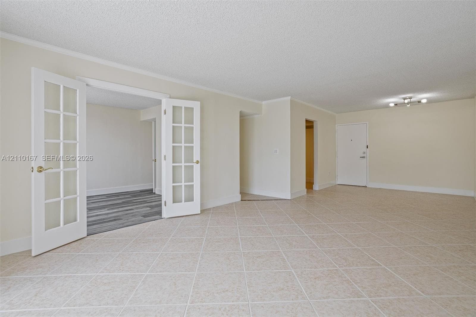 Neutral tile flooring in a diagonal pattern, interior French doors with glass panes, flush-mount lighting, and solid core doors