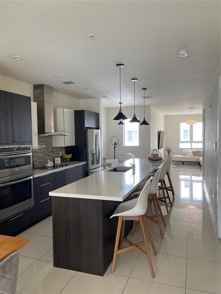 Kitchen featuring an expansive stone-surface island, stainless steel wall-mounted oven, built-in flat-panel cabinetry, stone-tiled backsplash, and recessed lighting