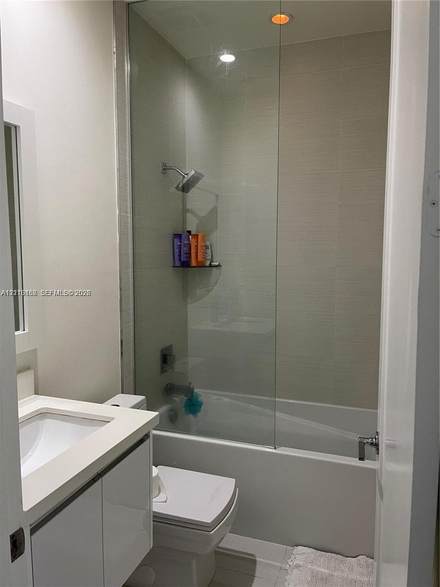 Bathroom featuring a white vanity with integrated basin, frameless glass shower panel, recessed ceiling lighting, and full-height tiled shower walls