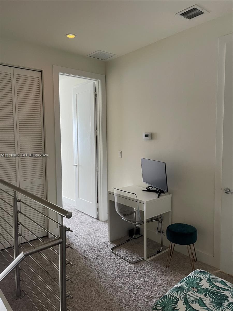 Interior space featuring neutral wall tones, carpeted flooring, louvered closet doors, and a metal railing system