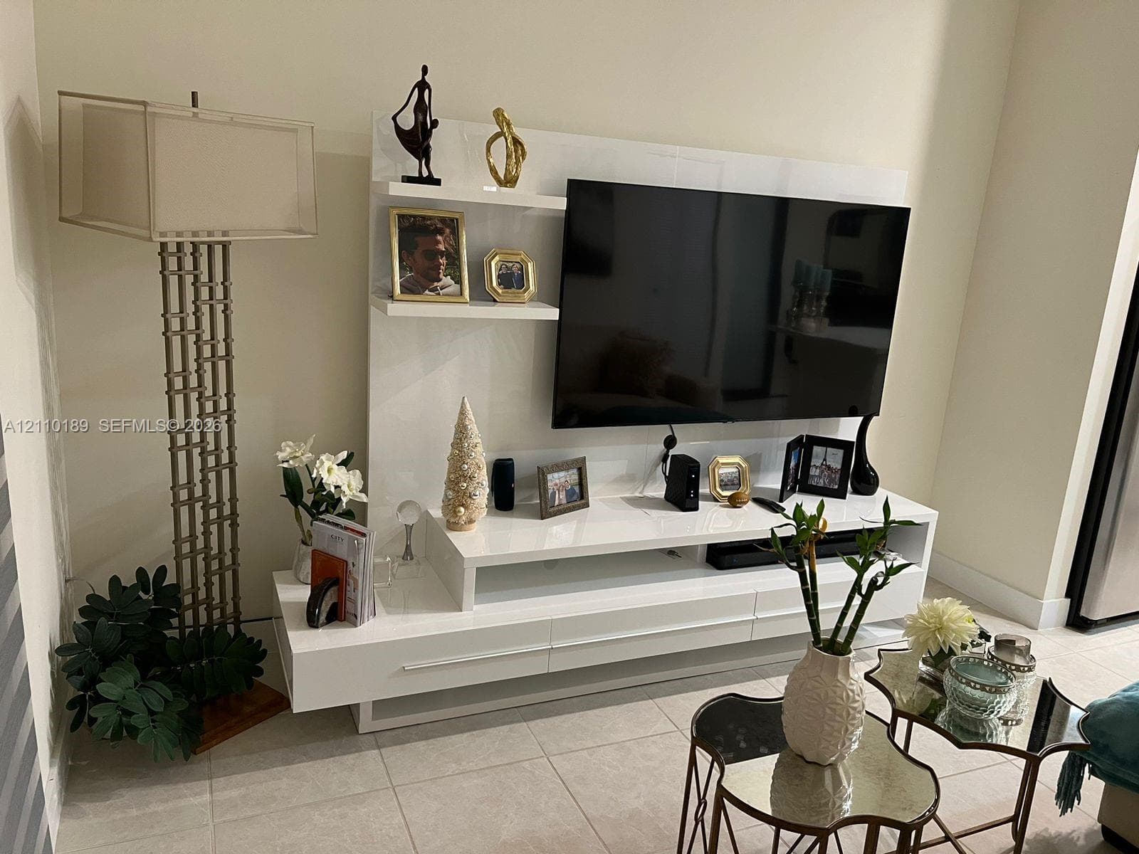 Glossy white built-in media console featuring integrated shelving and horizontal drawer storage, accented by neutral-toned tiled flooring