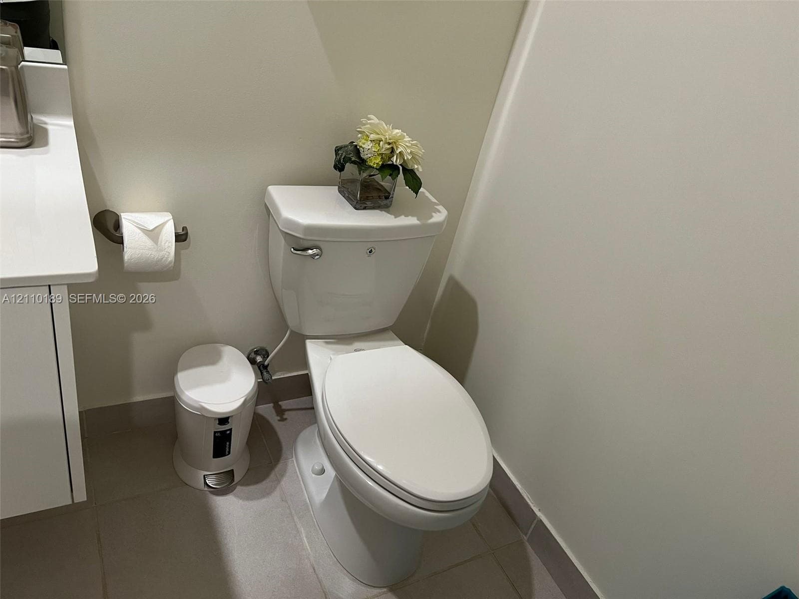 White bathroom featuring a solid-surface countertop with a vanity cabinet, chrome-finished hardware, and ceramic tile flooring