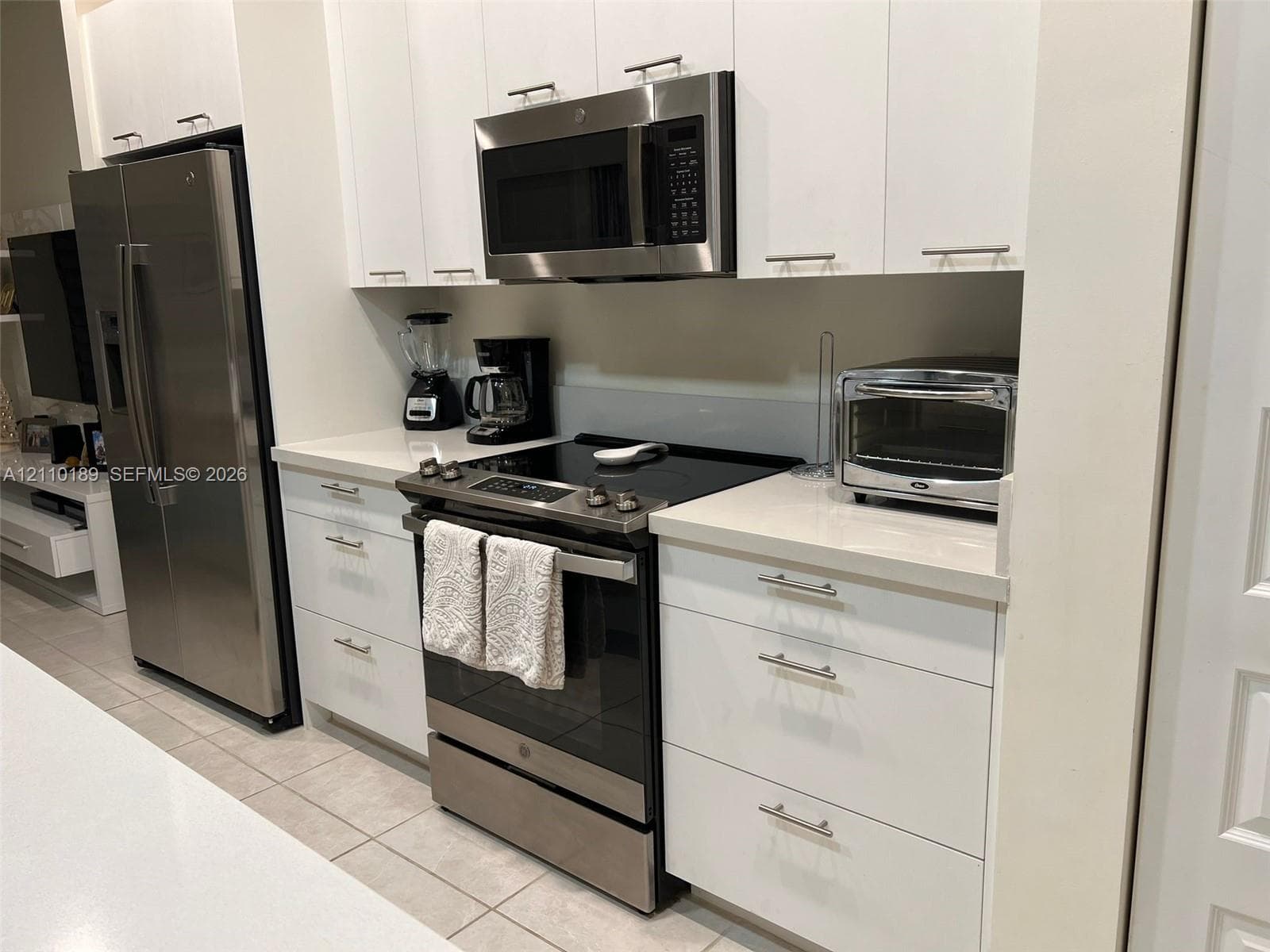 Kitchen featuring flat-panel white cabinetry, stone-finish countertops, stainless steel refrigerator, built-in microwave, and slide-in electric range