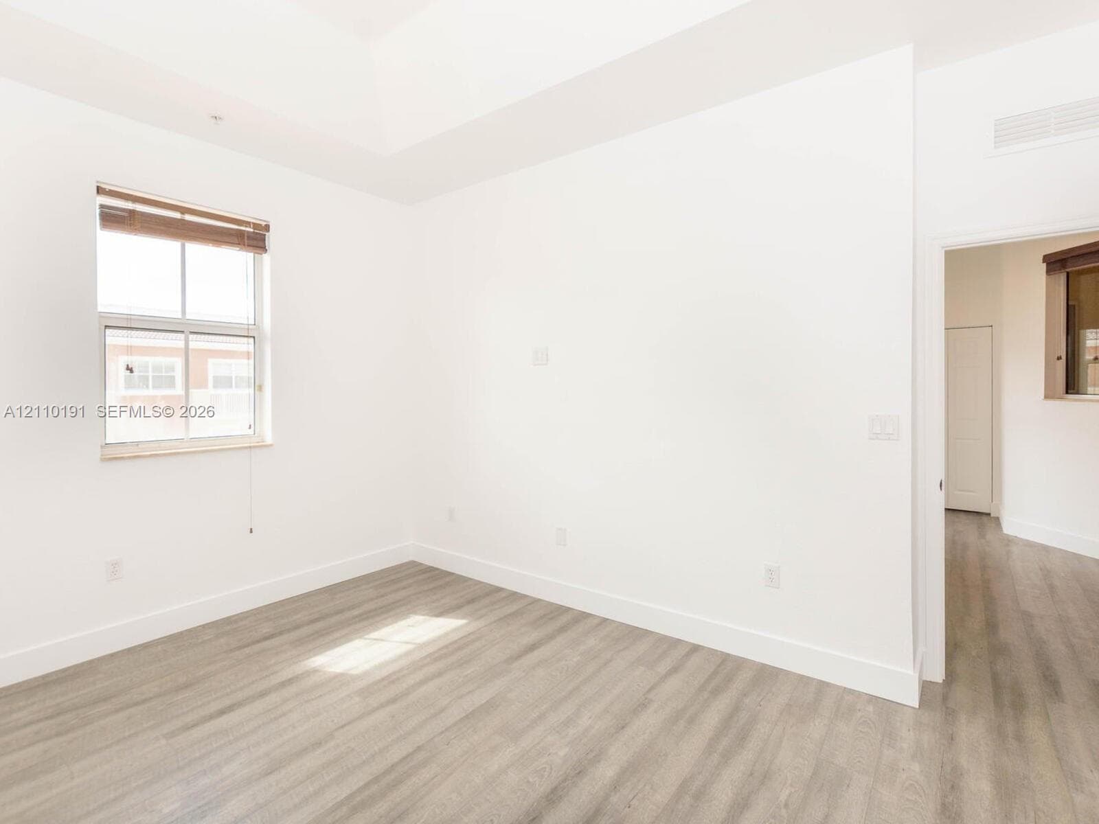Neutral-toned room featuring a tray ceiling, wood-finish flooring, and a window with blinds