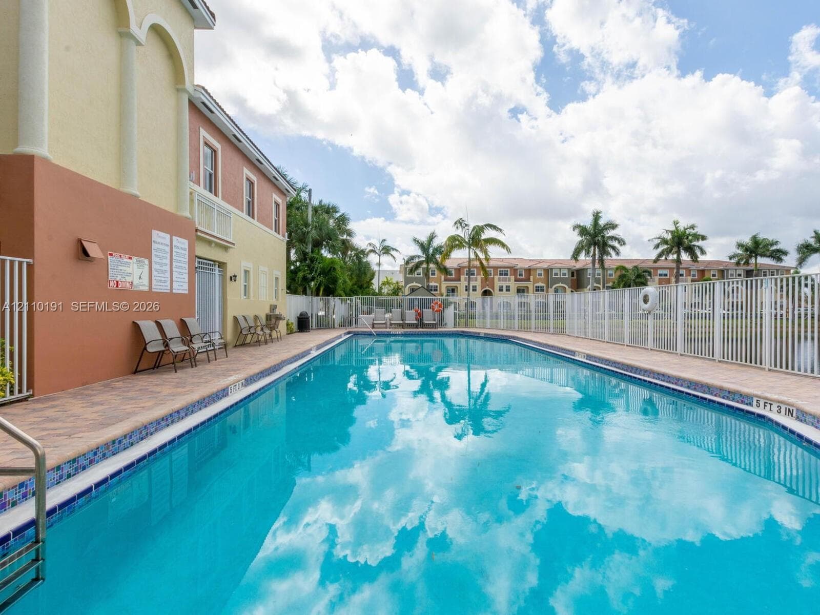 In-ground swimming pool featuring a tiled waterline, metal safety fencing, and paved deck surround
