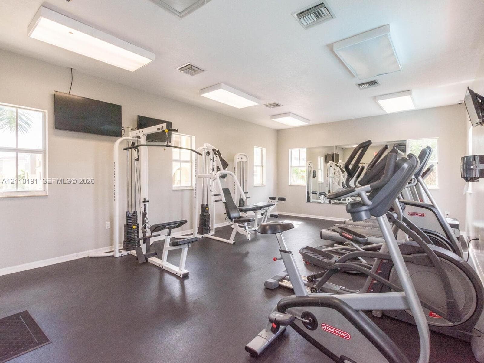 Fitness area featuring durable rubber flooring, wall-to-wall mirrors, recessed lighting, and multiple windows