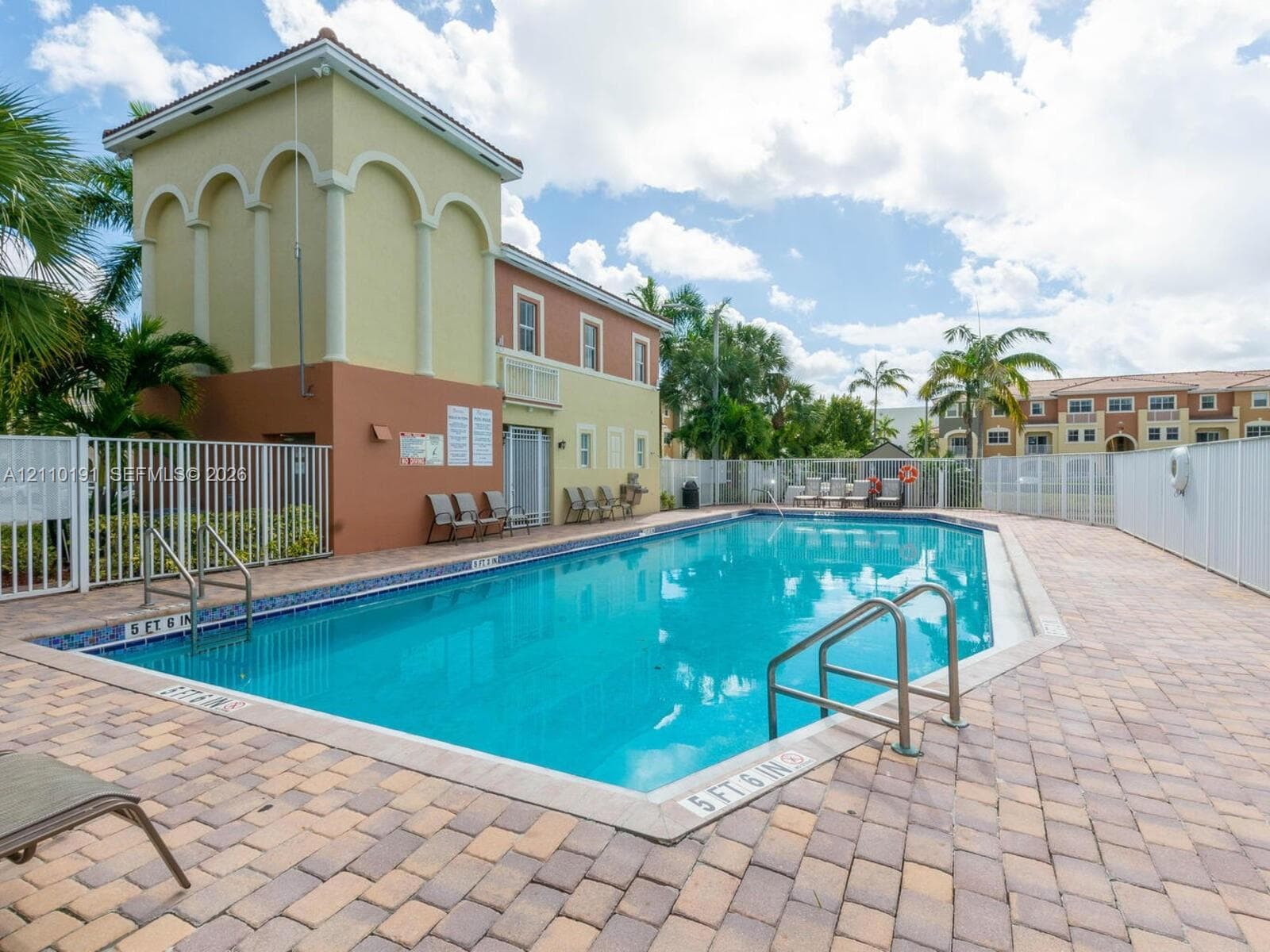 In-ground swimming pool featuring a paver deck, metal safety fencing, and stair entry access