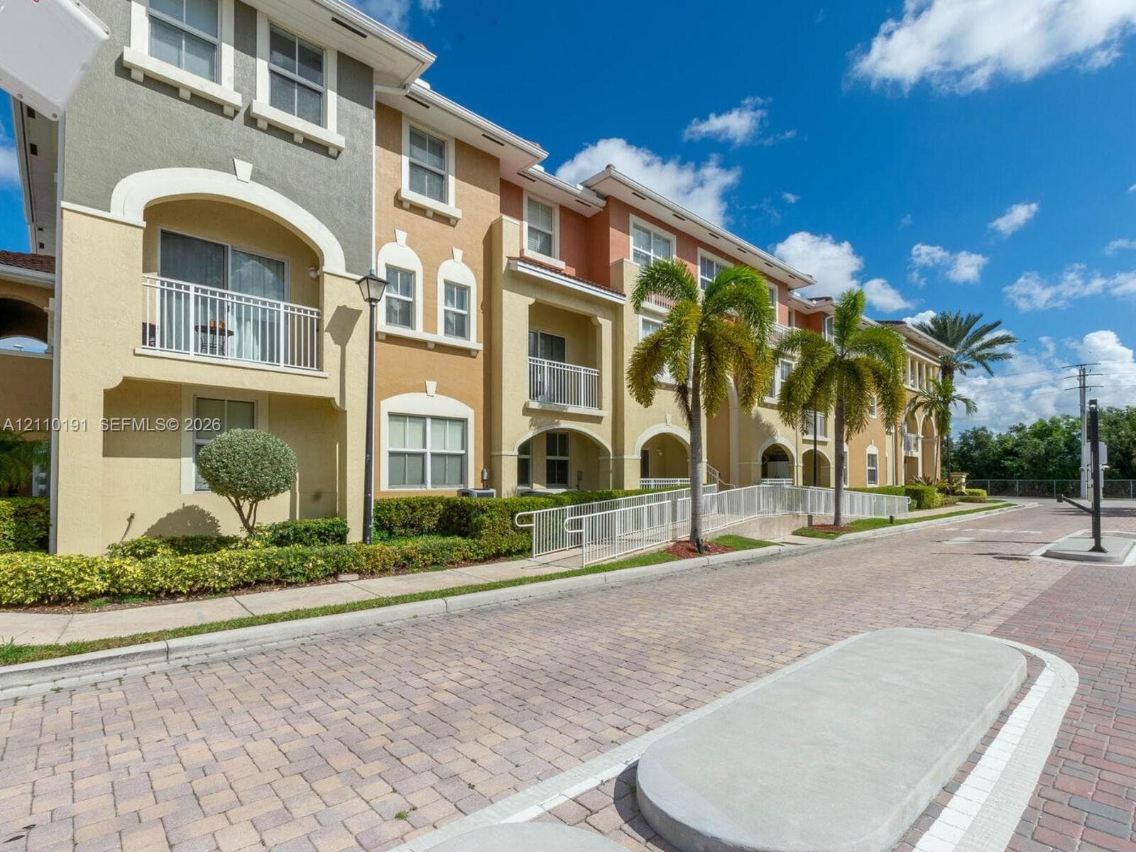 Multi-story exterior featuring arched architectural detailing, private balconies with white railings, textured stucco facade, and paver-stone driveway