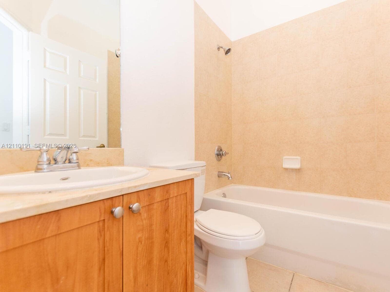 Bathroom featuring a wood-finish vanity with a stone countertop, an integrated drop-in sink, a wall-mounted mirror, and a bathtub with tile surround