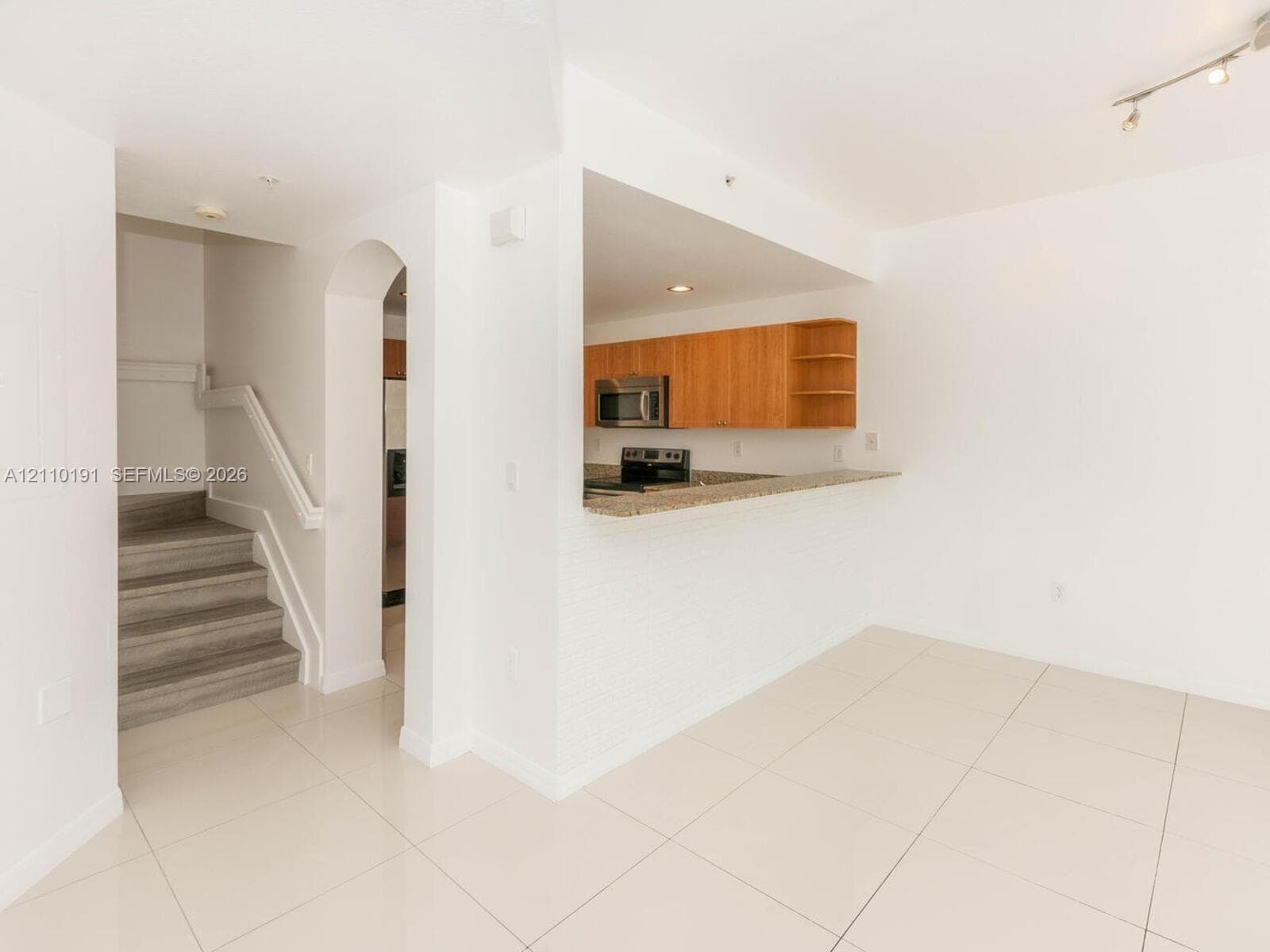 Kitchen featuring flat-panel wood cabinetry, stone-finish countertops, and stainless steel built-in appliances, complemented by a stone-tile floor and a structural arched entryway