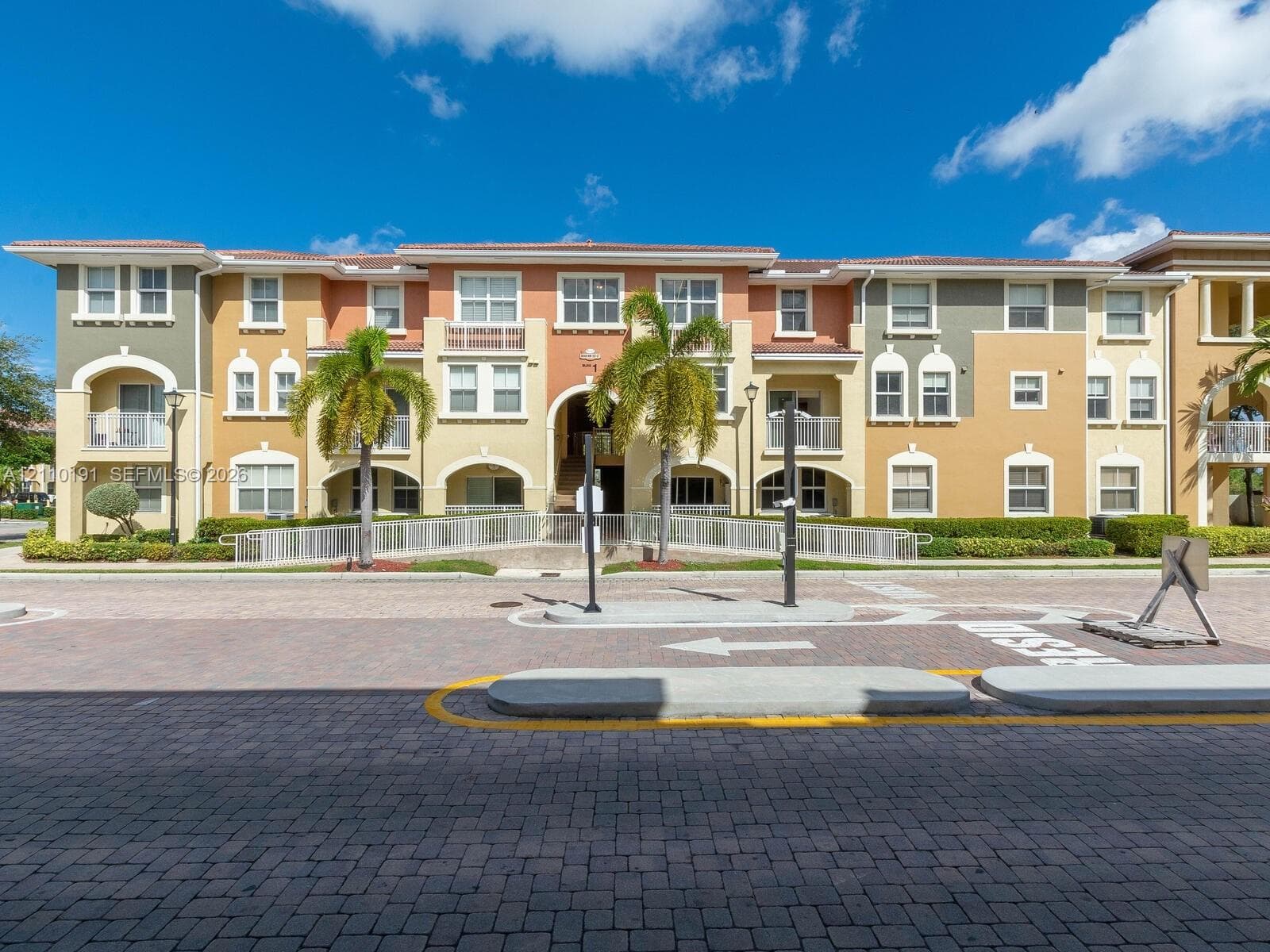 Multi-story Mediterranean-style exterior featuring a stucco facade, arched architectural detailing, private balconies with metal railings, and integrated palm tree landscaping