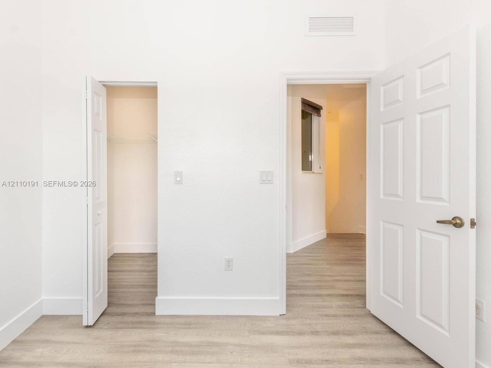 Room featuring wood-finish flooring, white walls, six-panel interior doors, and a built-in closet with wire shelving