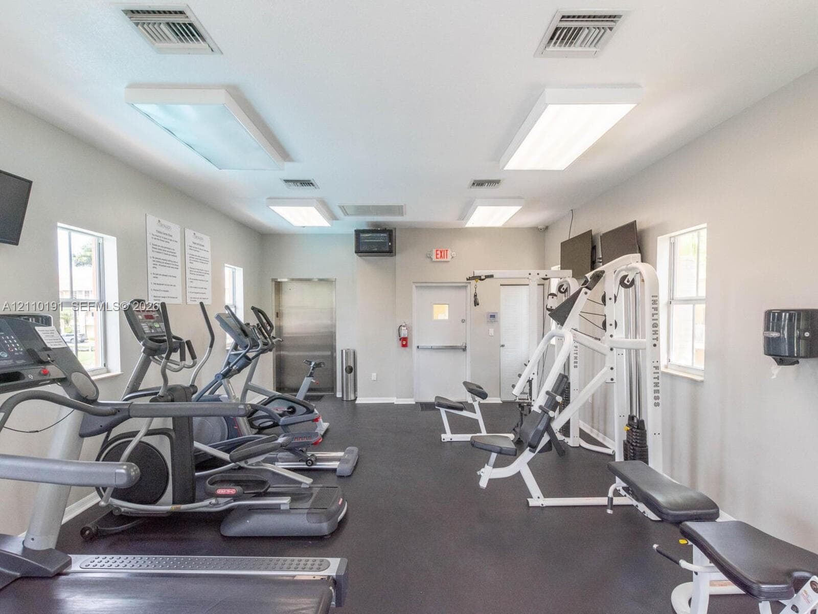 Fitness room featuring durable rubber flooring, multiple dual-pane windows, and high-output overhead lighting