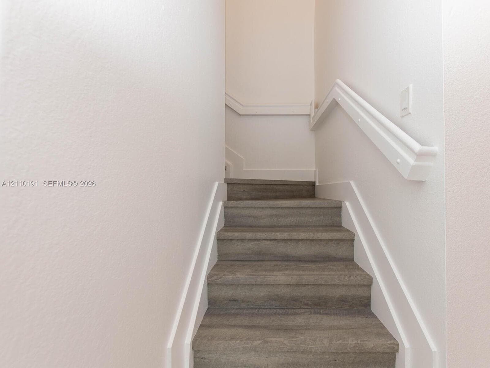 Staircase featuring wood-finish treads, crisp white trim, and a matching handrail