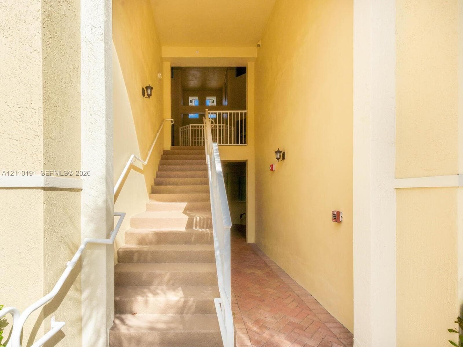 Exterior staircase featuring stucco walls, a herringbone-pattern brick pathway, and white metal railings