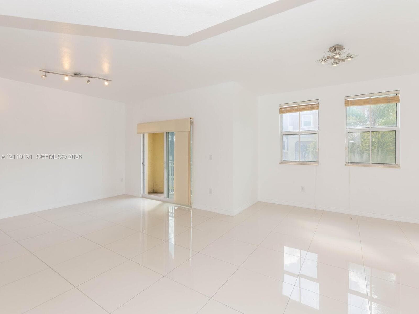 Open-concept space featuring polished ceramic tile flooring, recessed tray ceiling, multi-light track fixtures, and dual-pane windows