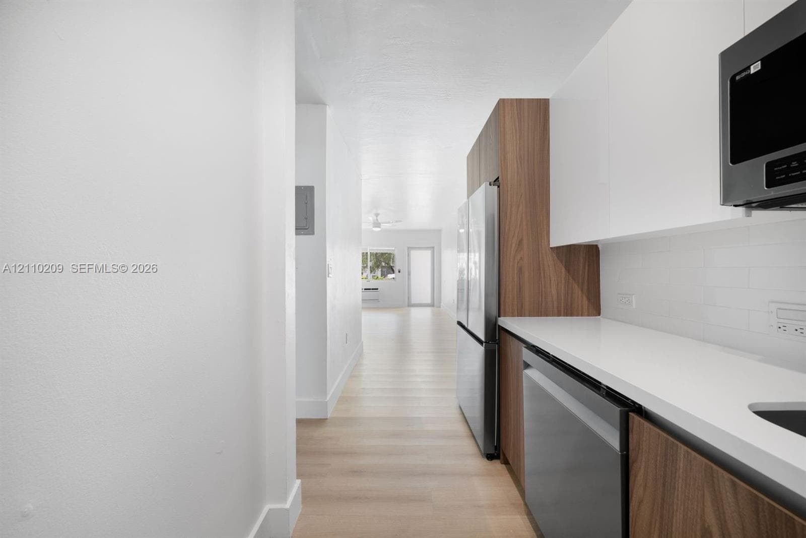 Kitchen featuring gloss-finish upper cabinetry, wood-finish base cabinetry, stainless steel appliances, solid-surface countertops, and white subway tile backsplash