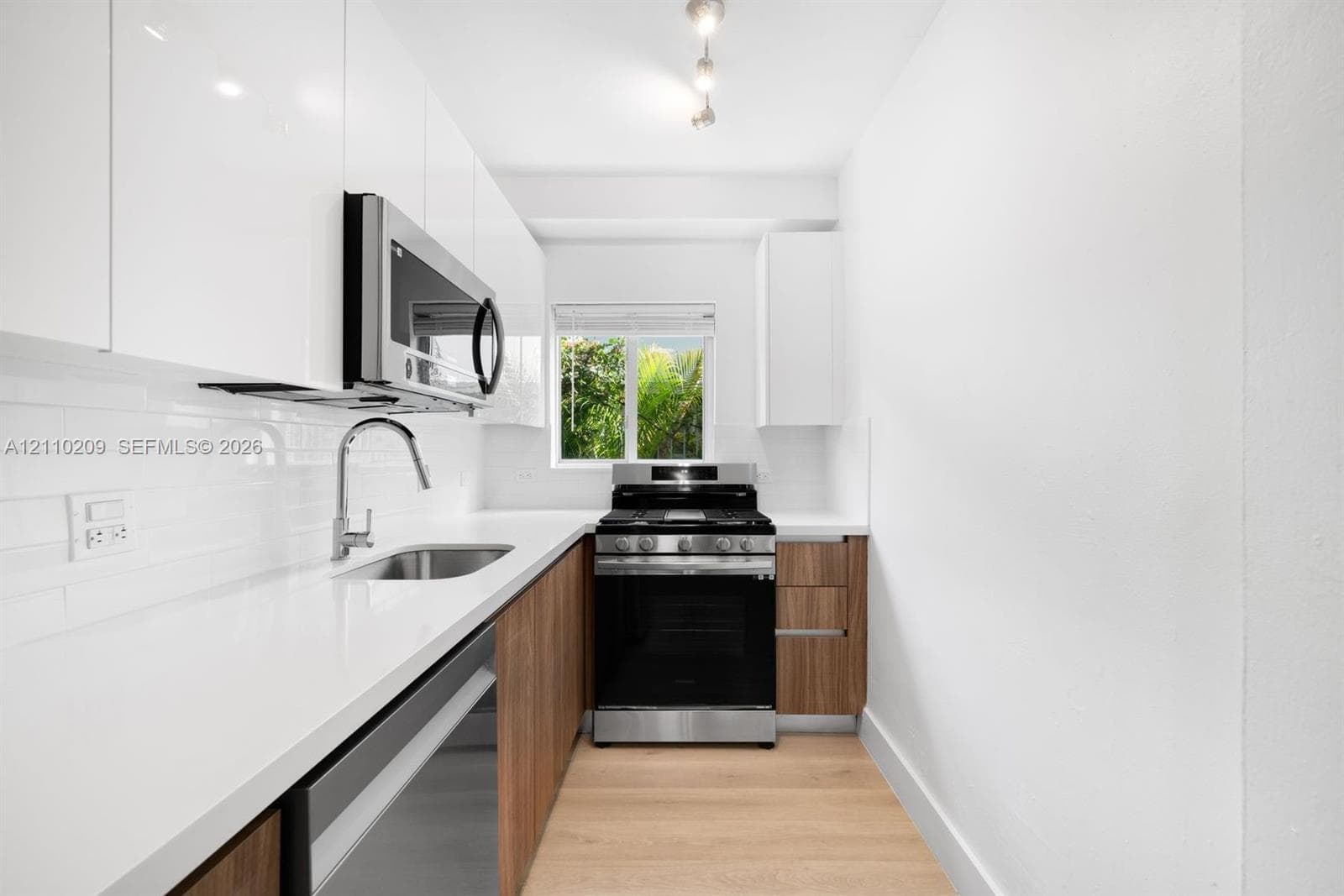 Kitchen featuring white gloss cabinetry, wood-finish lower cabinets, quartz countertops, white subway tile backsplash, and stainless steel appliances