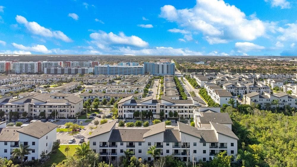 Aerial perspective of a multi-unit residential community featuring light-toned exteriors, pitched roofing, private balconies, and landscaped grounds