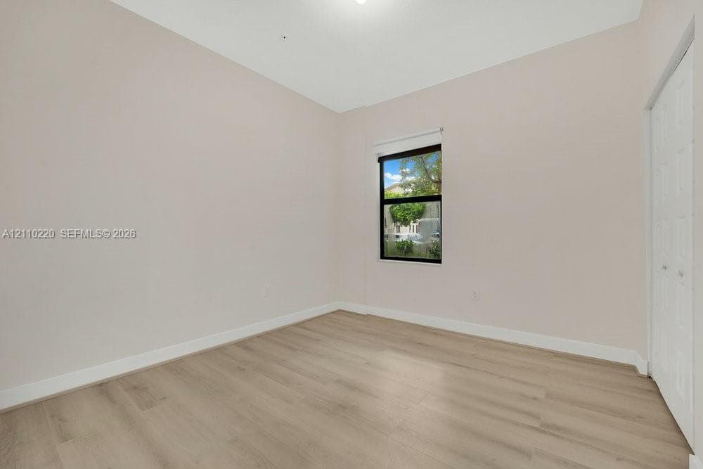 Neutral-toned interior space featuring wood-finish flooring, a single-pane window with black framing, and white bi-fold closet doors
