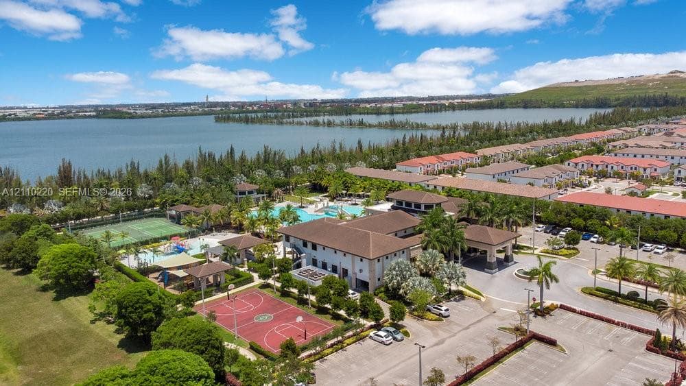 Aerial perspective of the community center featuring an outdoor swimming pool, tennis court, basketball court, and paved parking area