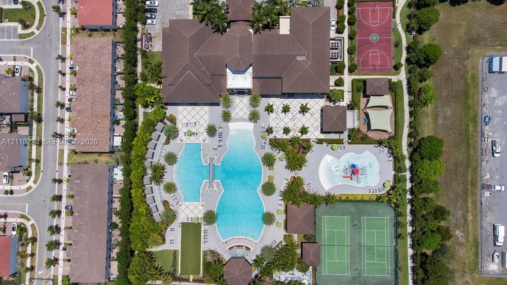 Aerial perspective featuring a large multi-section swimming pool, two tennis courts, a basketball court, and a splash pad within a landscaped complex