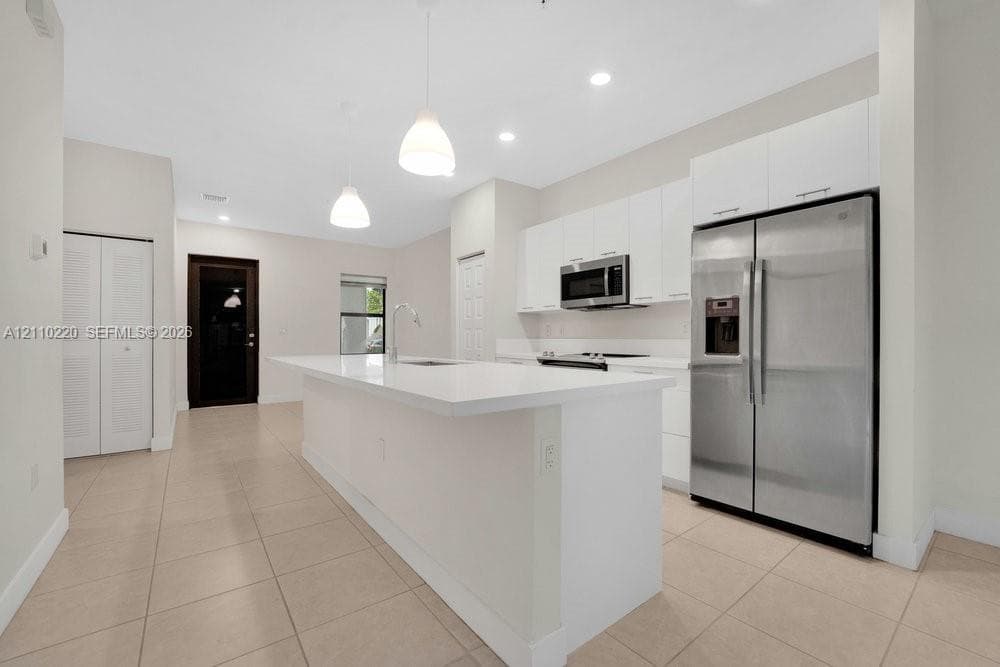 Kitchen featuring white flat-panel cabinetry, a central island with a quartz countertop, stainless steel refrigerator, built-in microwave, and tile flooring
