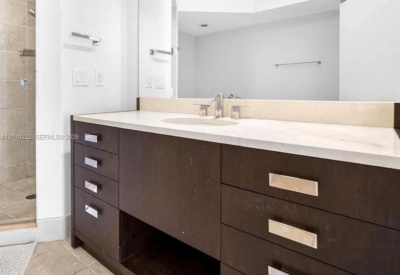 Bathroom vanity featuring dark wood-finish cabinetry, a neutral solid-surface countertop with an integrated oval sink, polished metal hardware, and a large-format mirror