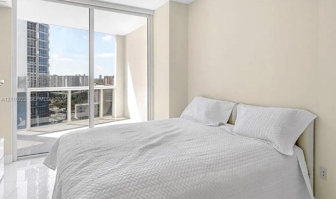 Floor-to-ceiling glass sliding doors, private balcony, neutral wall palette, and polished tile flooring