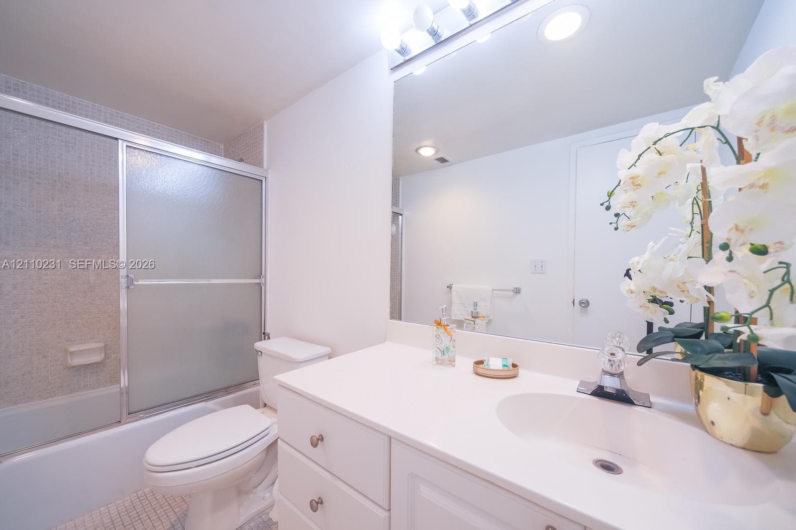 Bathroom featuring white vanity cabinetry, integrated countertop with a molded sink, polished chrome faucet, full-width mirror, and a shower-tub combination with a sliding glass door