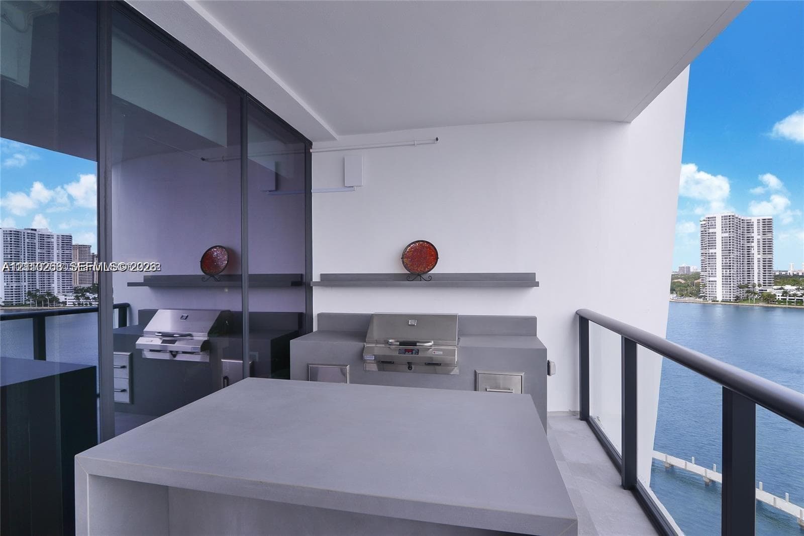 Covered balcony featuring a built-in outdoor kitchen with stainless steel grill, integrated storage, stone-finish countertop, and black metal railing