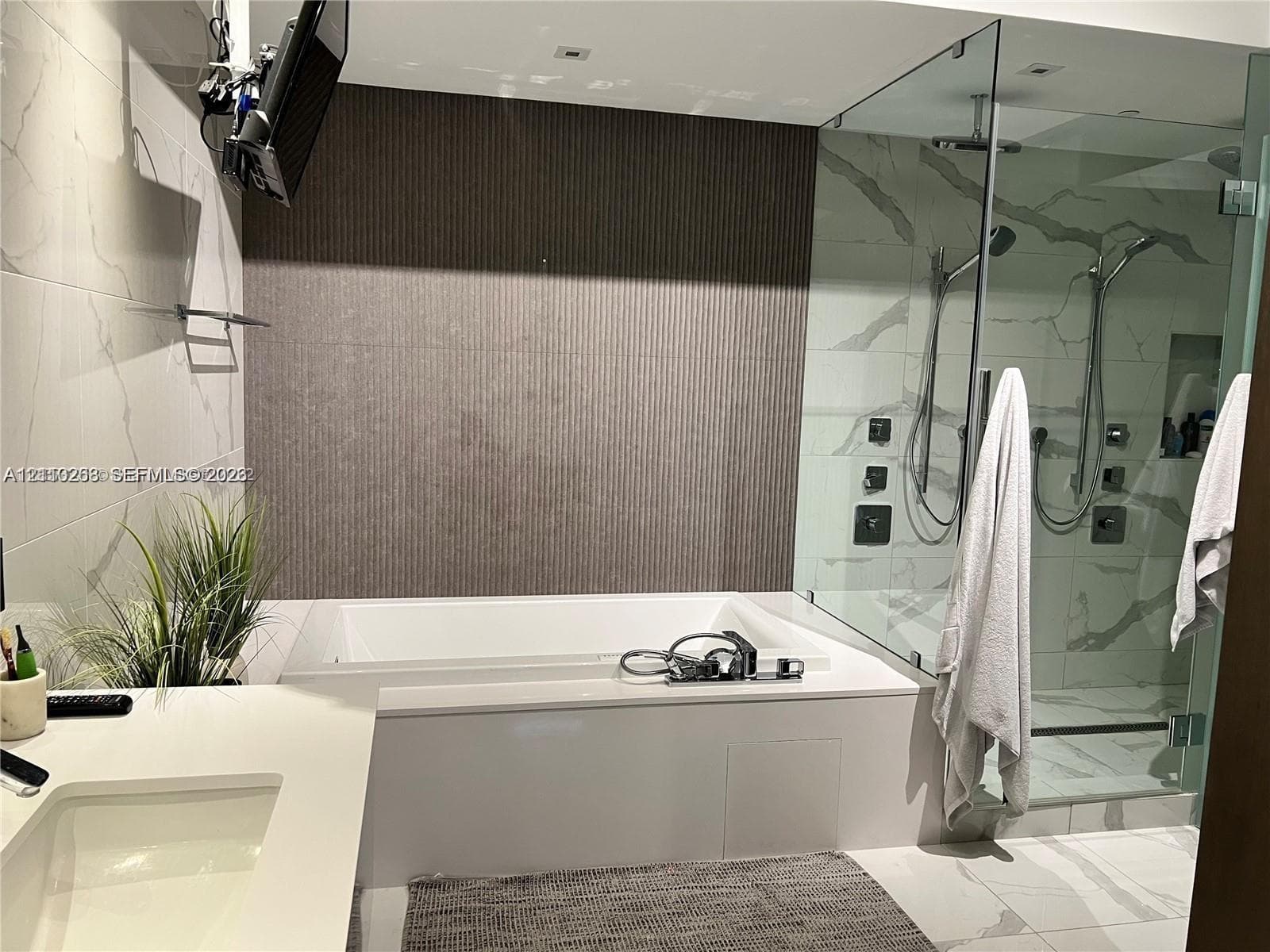 Soaking tub with a white composite surround, walk-in glass-enclosed shower featuring dual showerheads, textured accent wall, and stone-finish wall and floor tile