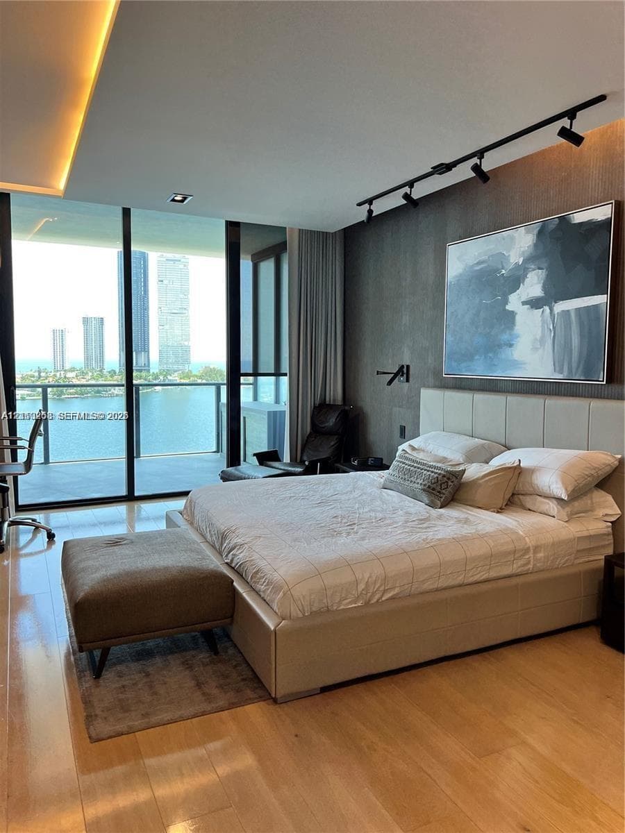 Floor-to-ceiling glass windows, wood-finish flooring, recessed tray ceiling lighting, dark textured accent wall, and track lighting