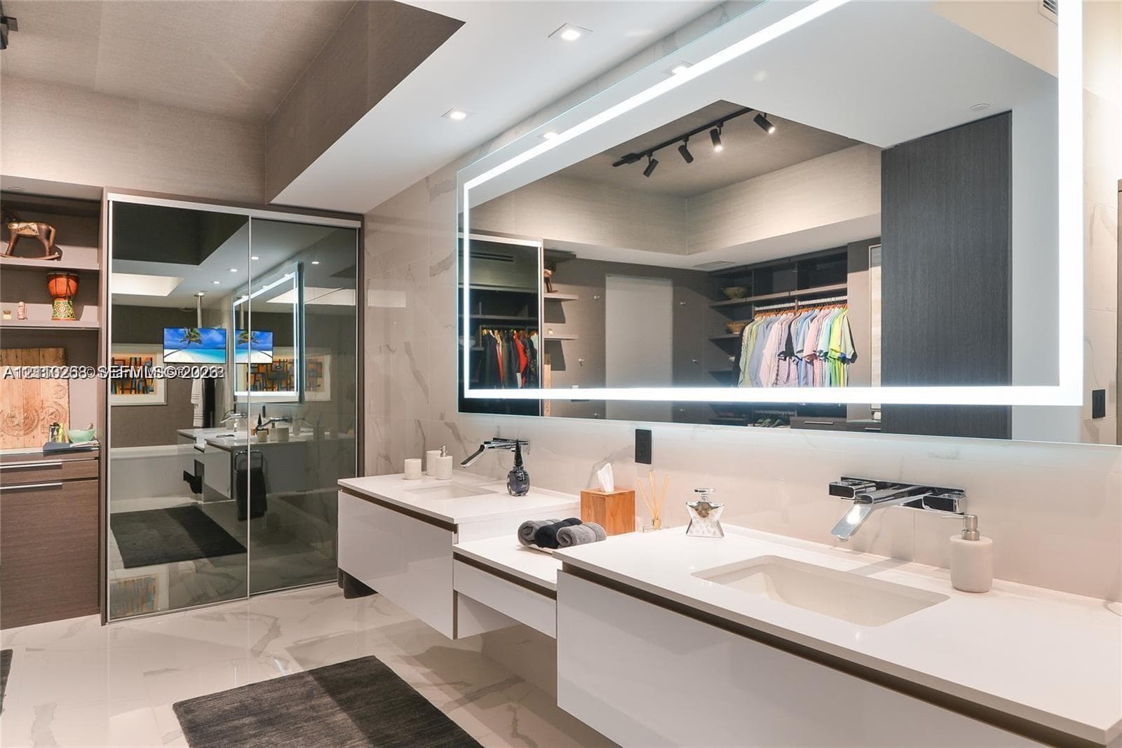 Double floating vanity with integrated rectangular sinks, expansive LED-backlit mirror, wall-mounted chrome faucets, and large-format porcelain tile flooring
