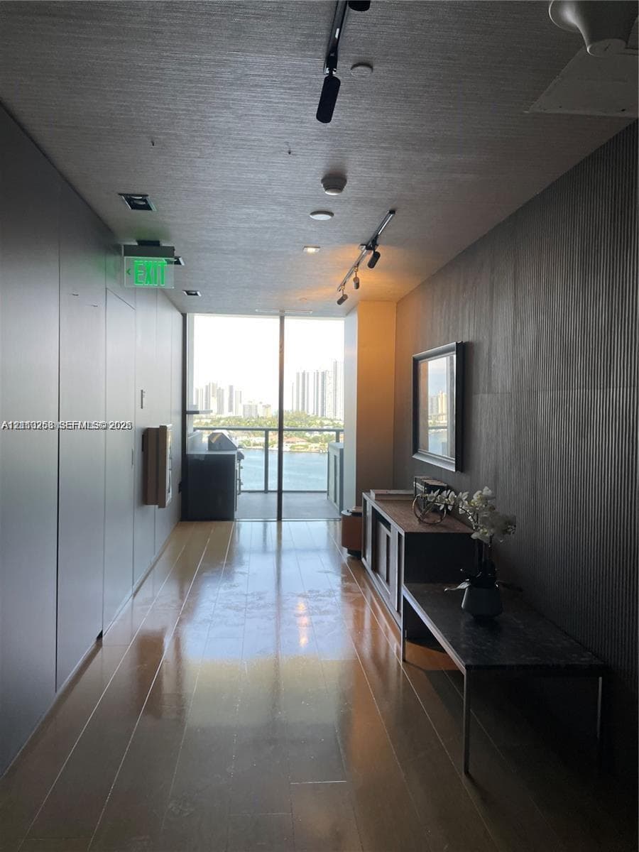 Entryway featuring floor-to-ceiling wood-finish wall paneling, polished wood-finish flooring, adjustable track lighting, and a full-height glass door opening to a balcony