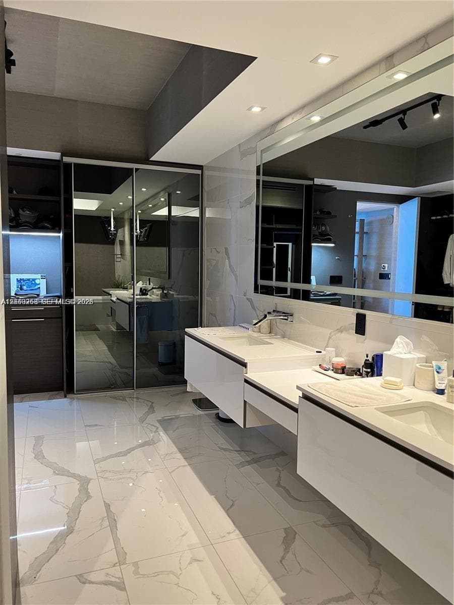 Floating double vanity with integrated sinks, large wall-mounted mirror, polished stone-finish flooring, and mirrored sliding-door cabinetry