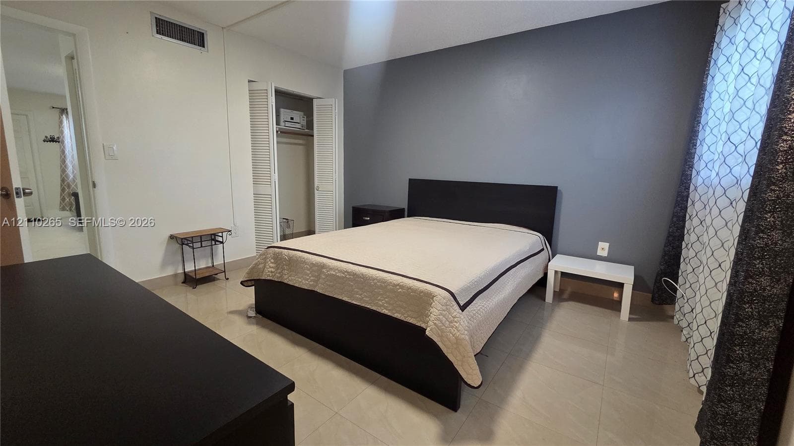 Room featuring neutral large-format tile flooring, a charcoal gray accent wall, and a double-door closet with louvered panels