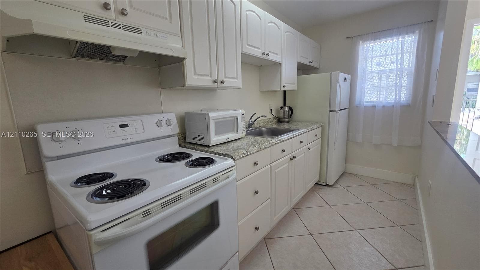 Kitchen featuring white cabinetry, stone-finish countertops, stainless steel sink, tile flooring, and integrated white appliances
