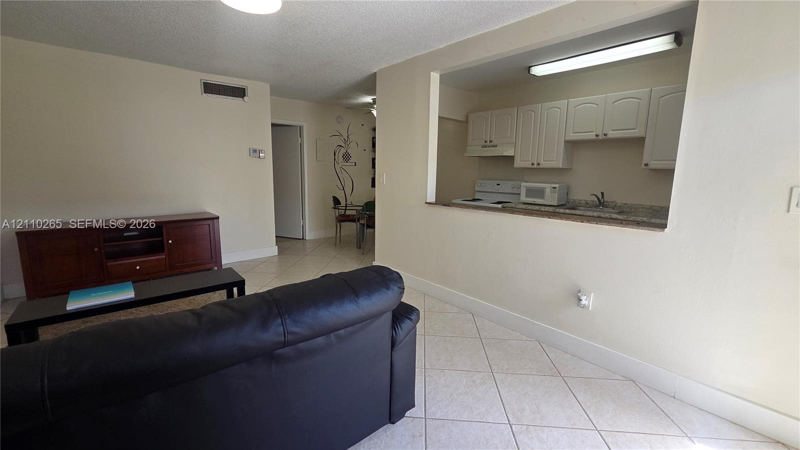 Open-concept interior featuring light-colored tile flooring, a kitchen pass-through, white shaker-style cabinetry, and a stone-finish countertop