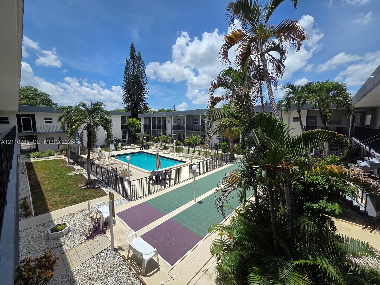 Outdoor recreation area featuring an in-ground swimming pool, perimeter metal fencing, a hard-surface game court, and mature palm trees