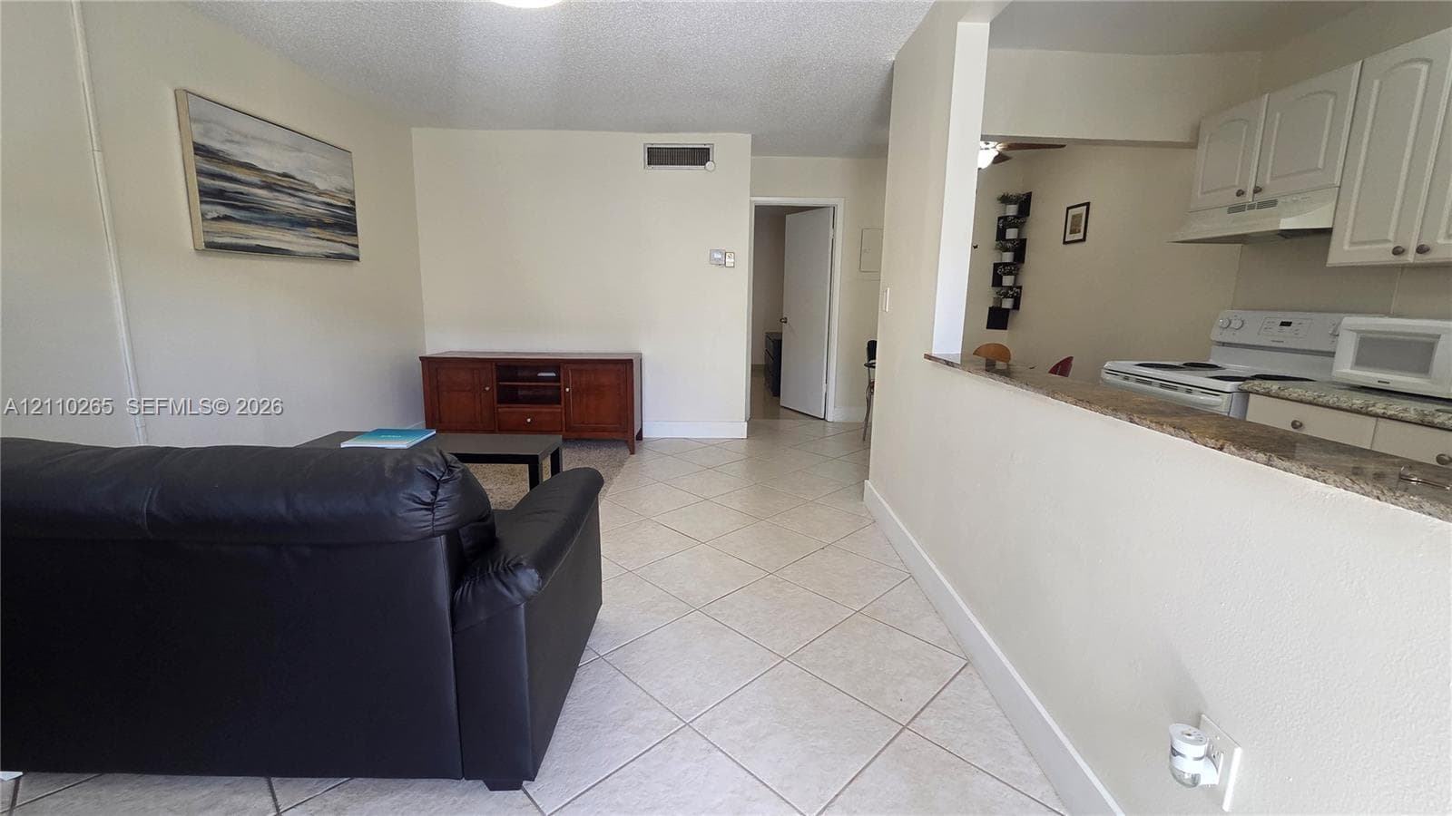 Interior featuring diagonal ceramic tile flooring, kitchen pass-through window with a stone-finish countertop, and white shaker-style cabinetry
