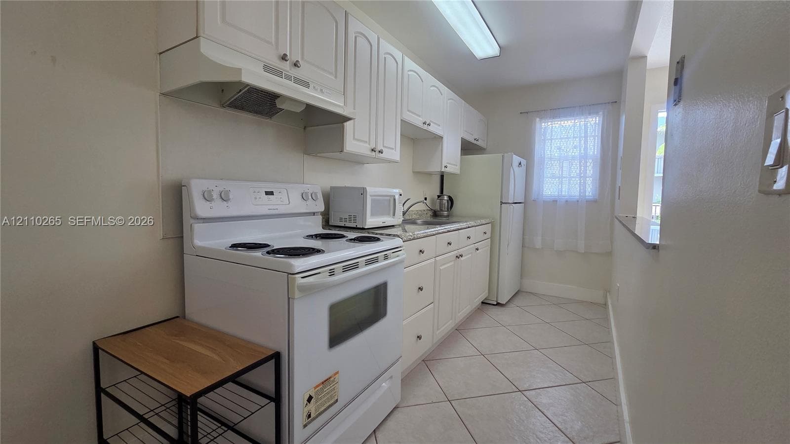 Kitchen featuring white cabinetry, stone-surface countertops, tile flooring, and integrated white appliances